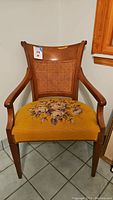 Full front view of wood framed chair showing woven cane backrest and needlepoint floral seat upholstery