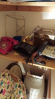 Wide view of shelf with multiple phones, accessories including an empty jewelry box and a metal frame stand, showcasing all lot contents.