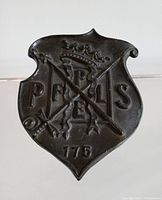 Front view of the antique bronze plaque showing crest with crown, crossed arrows, and the letters P F L S with number 175 below.