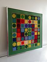 Angled front view of framed Op Art needlepoint artwork showing multicolored geometric design