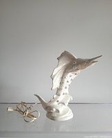 Full view of the white iridescent glazed swordfish ceramic mood lamp with its power cord and plug resting on a clear surface against a neutral background.