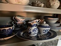 Blue Willow china including cups, saucers, creamer, sugar bowl on a shelf.