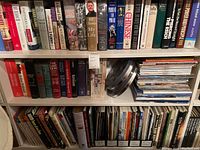 View of bookshelf with political and historical books, including biographies and power politics titles, and a collection of war history magazines stacked horizontally with metal film reels.