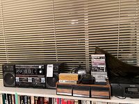 Wide view of lot on countertop with GE dual cassette boom box, Sony CD player radio, cassette tapes and CDs, audio cleaner, and wood drawers.