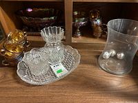 Shelved collection of carnival glass cups, bowls, and a large carnival glass serving tray alongside a clear glass vase containing three silver balls.