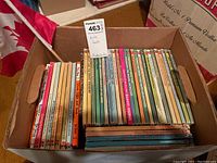 Box filled with multiple thin children's books, spines show a variety of classic tales and Disney stories.