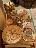 Overview of assorted vintage porcelain serving items showing covered dishes, pitchers, plates and decorative bowls with floral and landscape designs.