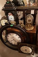 Overall view of multiple clocks on table and shelf including anniversary clock, wooden mantel clocks, wall clocks, and smaller alarm clocks
