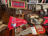 Photo showing Coca-Cola branded lamp, tray, bar mirror, and pennants arranged together