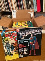 Open cardboard box with comic books inside, featuring Marvel's Wizard of Oz and Superman: The Movie album visible on top.