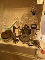 Overview of crystal and silver plated sterling items including decanter, glassware, ink wells, door handle, and small containers with ornate silver lids and bases.