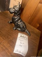 Front angled view of the black dog figurine piggy bank showing detailed fur texture and a red collar, placed on a wooden surface.