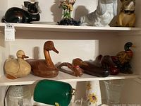Shelf showing seven duck figurines and decoys of wooden and ceramic construction, varying colors from light tan, browns to multicolored ceramic.