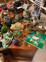 Overview of all frog figurines and collectibles arranged on a wooden surface showing multiple ceramic, glass, and metal frog-themed items.