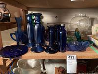 Blue glass vases, plates, candlesticks, and other glassware on a shelf showing various blue tones and shapes