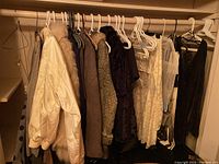 Hanging rod with 10 assorted ladies coats, jackets, and dresses on plastic hangers, including a cream satin bomber jacket with fur collar and darker coats