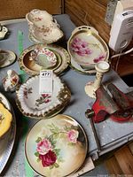 Various Limoges and floral porcelain serving dishes and plates with gold trim arranged on a table including scalloped edges and floral decorations.