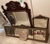 Four vintage mirrors displayed including large wooden frame mirror with carved detail, rectangular gold-tone framed mirror, small rectangular ornate mirror, and oval bamboo framed mirror