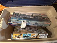 Open tote showing stack of model kits including USS Ingersoll and jets model kits with brand logos Dragon and Hasegawa visible