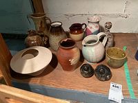 Photo showing full lot with various pottery pitchers, vases, bowls and ceramic figurines arranged on a wood surface against a wall.