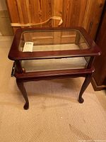 Full view of the wooden side table with glass inset top and cabriole legs, showing the finish and overall structure.