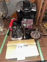 Photo showing the Keurig coffee maker, Dirt Devil hand vacuum, hair dryer, jewelry cleaner, manual coffee mill, and a closed box possibly containing other items.