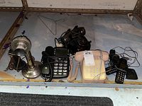 Wide shot showing all telephones arranged on a shelf, featuring candlestick phone, pushbutton phones, and cordless phones.