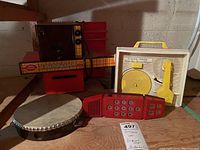 Wide view showing all four items: Easy Bake Oven, Fisher Price Music Box Record Player, Merlin Electronic Wizard game, and tambourine on a wooden surface