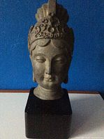 Front view of vintage Asian bust sculpture showing facial features and headdress on wooden base.
