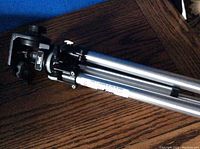 Side view of tripod head and upper leg section with adjustment knobs visible, showing aluminum and black metal construction.