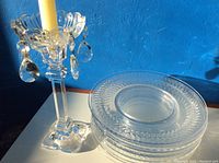 Photo of tall clear crystal candle holder with yellow taper candle and stacked clear etched crystal salad plates with intricate rim pattern.