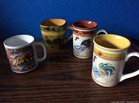 Four ceramic cups with rooster and New Mexico themed designs positioned on wooden table background.