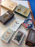 Photo showing six vintage decks of playing cards arranged on a surface, including floral, musical instruments and patriotic themed boxes.