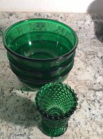 Photo showing three translucent emerald green glass bowls stacked and a hobnail textured emerald green glass footed candle holder placed beside them on a granite countertop.