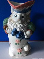 Front view of the vintage Fitz and Floyd ceramic cat figurine showing facial features, tricorn hat, green sleeves, and a blue umbrella