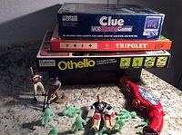 Stack of three vintage board games with several toy figures and red plastic toy gun arranged in front on a granite counter.