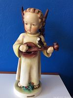 Front view of the vintage Hummel angel figurine showing mandolin and bird details against a blue background.