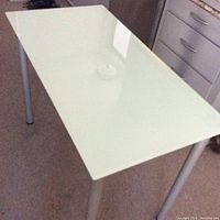 Top-down view of white glass tabletop and metal legs showing clean, unblemished surface and screw-on leg attachment.