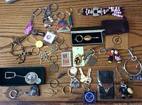 Wide view showing an assortment of 27 assorted vintage keychains including chain links, boxed items, carved stones, beads, and metal designs with logos and figurines.