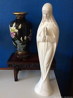Madonna statue, cloisonné vase on wood base, and wood display table against blue background
