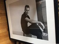 Framed black and white photo of young man sitting barefoot, clearly showing the image and framing details.