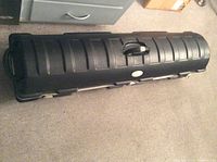 Full closed view of the long black plastic golf travel case showing its length, ribbed design, central handle, and metal latches.
