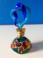 Perfume bottle upright showing multicolor body and blue decorative stopper on top with gold neck.