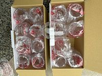 Two open boxes containing eight individually plastic-wrapped clear wine glasses each, shown inside the boxes on a flat surface.