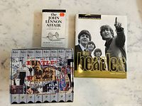 Photo showing 7 Beatles VHS tapes and 3 Beatles-related books including The John Lennon Affair and The Beatles Complete Illustrated Story