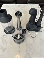 Full kit with hand mixer in charging base and all attachments arranged on marble surface