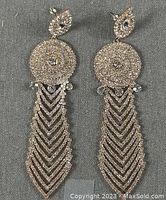 Front view of gold tone chandelier earrings with intricate sparkling rhinestone design on gray background.