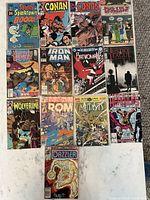 Photo shows all 13 comic books laid out in rows, identifiable titles including Spooky Spooktown, Conan, Justice League, Iron Man, Wolverine, Rom, Mutants, Hercules, and Dazzler.