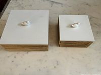 Top view of both wooden decor boxes showing white lids with bird figurines and natural wood sides.