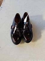 Top view of new women's dark polished leather Dr Martens shoes with buckle straps, placed side by side on a white surface.